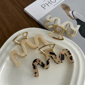 Three wavy acetate hair claws in cream, beige, and tortoiseshell on a ceramic tray