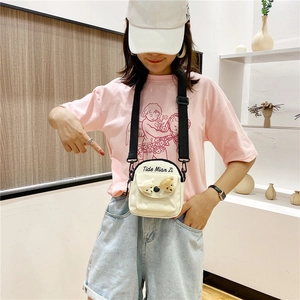 Detail of cream white canvas crossbody bag featuring two cute plush bear heads decoration