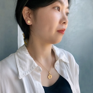 Detail of model wearing golden apple necklace and earrings with star cutout pattern