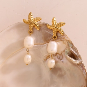 Detailed close-up of 18K gold starfish earrings with baroque pearl drops on a shell
