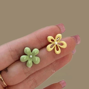 Close-up of elegant floral earrings in green and yellow colors held by hand