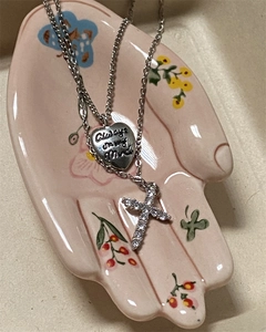 Silver multilayer necklace with engraved heart pendant and cross on a ceramic hand tray