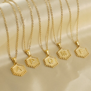 Detail of 18K gold-plated hexagonal initial necklaces on elegant golden silk fabric