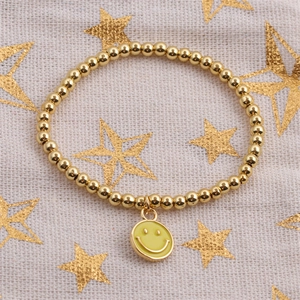 Detail of gold beaded bracelet featuring a yellow enamel smiley face charm and metallic beads