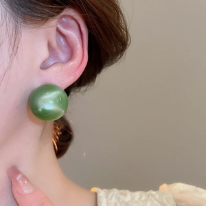 Close-up of a model wearing a glossy green round cat-eye stone stud earring