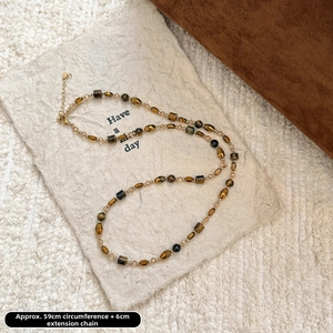 Détail du collier de perles en œil de tigre vintage sur un support en carton crème