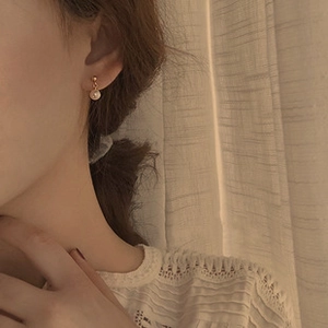 Model wearing baroque pearl stud earrings with gold metal accents in a home setting