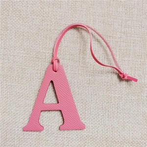 Pink lychee grain leather letter A bag charm with matching strap on linen background