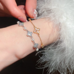 Detail of silver pearl clover bracelet and gold clover charm on wrist with feathers