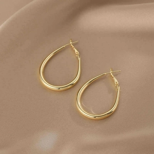 Detailansicht minimalistischer goldener ovaler U-förmiger Creolen auf Seidenstoff.