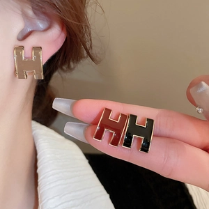 Close-up of enamel H-letter stud earrings in beige, red and black with gold finish