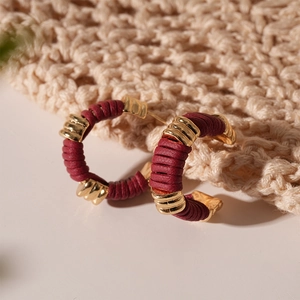 Détail macro de boucles d'oreilles C dorées avec enveloppe en cuir bordeaux texturé