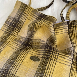 Detail of yellow and brown plaid woolen tote bag with bronze metal brand plaque