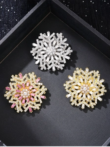 Detailed macro view of three 3D snowflake brooches in gold and silver with inlaid crystals