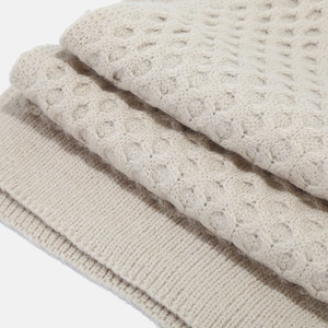 Detail of beige knit fabric featuring honeycomb texture and ribbed edge finish