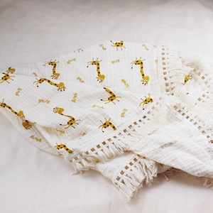 Detail of soft muslin baby blanket with giraffe print and decorative tassel edge