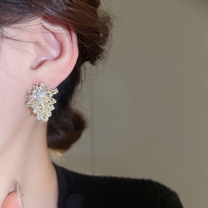 Close-up of elegant gold leaf-shaped earrings with sparkly crystals on a model's ear