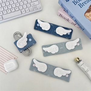 Denim cable organizer with plush wings and snap buttons on a white desk background