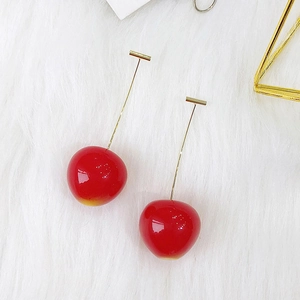 Detail view of realistic cherry earrings with resin red fruit and gold-tone stems on plush