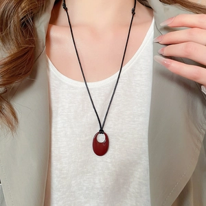 Gros plan du collier avec pendentif ovale ajouré rouge foncé sur un cordon noir
