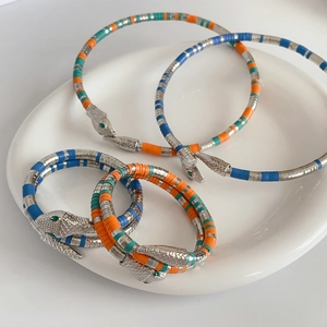 Close-up of three snake-shaped multi-color beaded wrap bracelets on a white ceramic plate