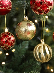 Detail of red and gold Christmas ornaments hanging on a festive tree with warm lights