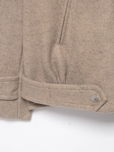 Close-up of brown wool bomber jacket featuring a metal button and side pocket detail