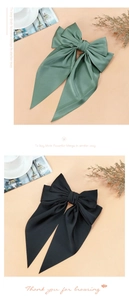Detailed view of large dark green and black satin bow hair clips on elegant background