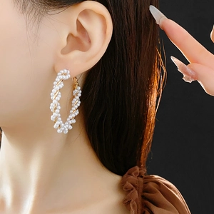 Detail of elegant gold-tone pearl wrap hoop earrings worn by a model in a side profile