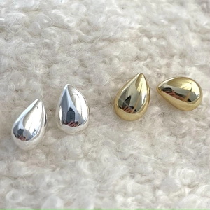 Teardrop stud earrings in gold and silver finish on soft white plush background
