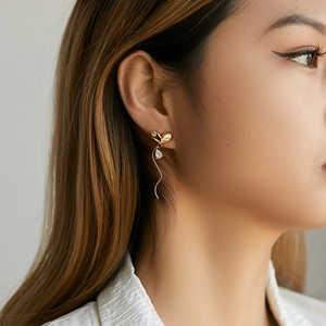 Close-up of golden heart earrings with wavy line and clear teardrop crystal on model