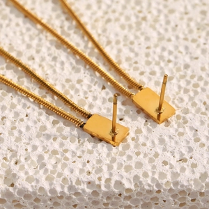 Macro shot of gold-plated stainless steel studs with delicate fringe chains on stone