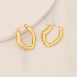 Macro di orecchini geometrici in oro lucido su vassoio di ceramica bianca