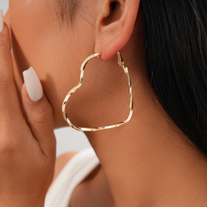 Close-up of a model wearing a large golden heart-shaped hoop earring with twisted design