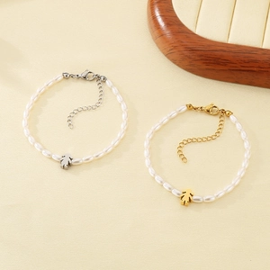 Detail of 4mm glass pearl bracelets with silver and gold girl pendants on a textured surface