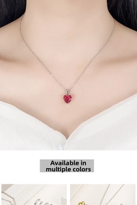 Detail view of a model wearing a heart-shaped red gemstone pendant on a thin silver chain
