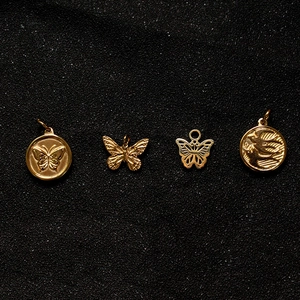 Golden butterfly and bird relief pendants set on black sand background for DIY jewelry