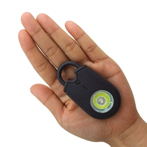 Portable personal safety alarm in hand, compact black device with green glow button