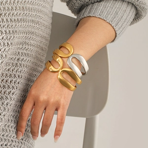 Stack of gold and silver stainless steel open bangles on a gray knit sweater background