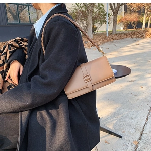 Detail of tan rectangle flap bag with a unique thick braided shoulder strap outdoors