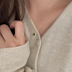 Detail of vintage gold necklace featuring an emerald green pendant on a knit cardigan