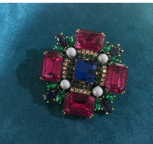 Close-up of vintage gold brooch with pink rhinestones, blue gems, and pearls on velvet