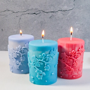 Drei farbige Stumpenkerzen mit Blumenrelief werden in minimalistischem Dekor angezündet