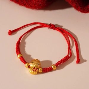 Detail of red braided lucky bracelet featuring a golden cartoon charm and beads