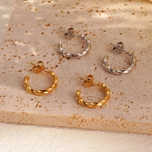 Minimalist twisted hoop earrings in gold and silver finish on textured stone background