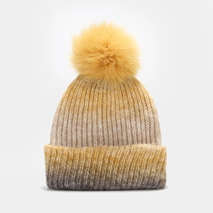 Détail du tricot épais dégradé et du grand pompon en fausse fourrure jaune sur le bonnet