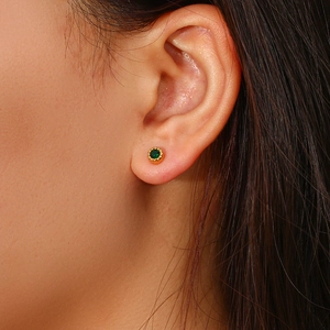 Close-up of a gold stud earring featuring a round green gemstone on a model ear