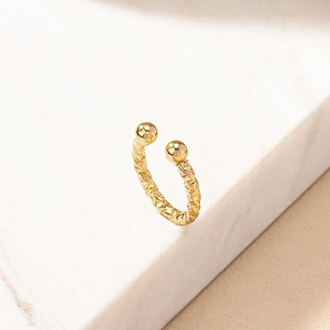 Minimalist gold twisted ear cuff with polished metal balls on marble background