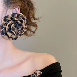 Macro side view of large leopard print fabric flower earrings worn by a model
