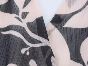 Detail of V-neckline on floral chiffon dress with black leaf print on beige fabric